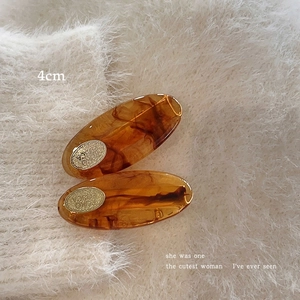 Close-up of 4cm amber tortoiseshell acetate hair clips with gold logo on plush fabric