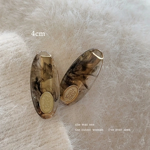 Detail view of 4cm acetate hair clip with black smoke ink pattern and gold metal tag