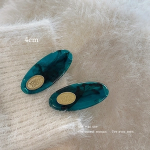 Close-up of 4cm dark green acetate hair clips with golden oval metal emblem detail