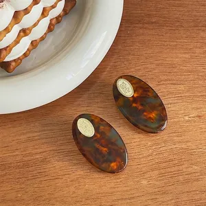 Chic tortoiseshell acetate hair clips with gold logo accents on a wooden background