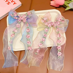 Macro detail of embroidered organza bow clips with golden edges and floral vines