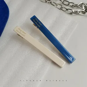 Close-up of beige and navy acetate duckbill hair clips with gold metal base