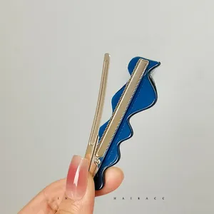 Detail view of blue wavy acetate hair clip with silver metal duckbill base held by hand