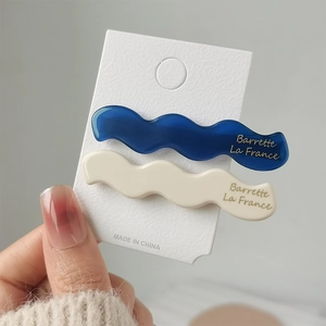 Detail showing blue and white wavy acetate hair clips with gold lettering on a card