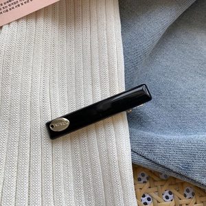 Detail of a sleek black acetate hair clip with a luxury gold metal brand plate