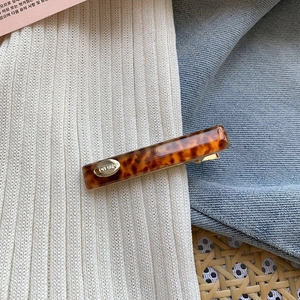 Detail of tortoise shell acetate hair clip with golden oval emblem and metal spring clip