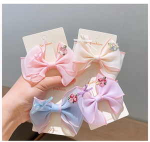 Detailed view of four handmade embroidered organza bow hair clips on a display card
