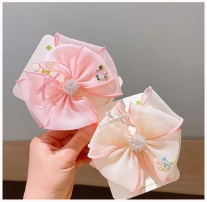 Close-up of pink and beige organza bow hair clips with floral embroidery and rhinestones