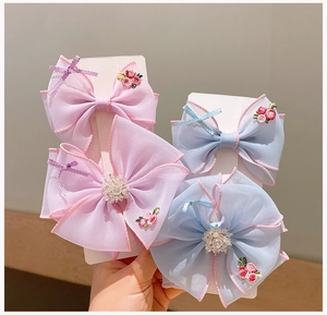 Close-up of embroidered mesh bow hair clips with delicate bead centers and pink stitched edges