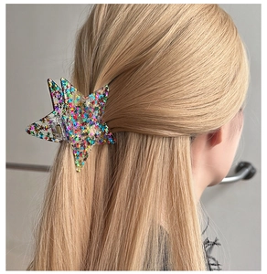 Detail shot of a star-shaped hair claw with colorful glitter sequins in a half-up hairstyle