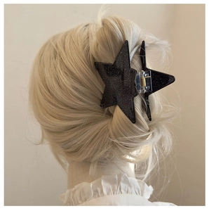 Detail of a large black star hair claw clip with a glitter matte finish on blonde hair