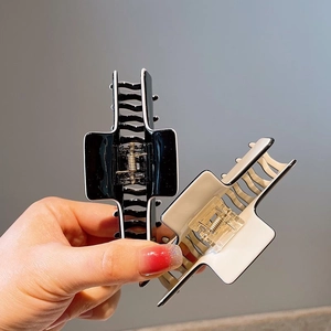 Detail of minimalist cross-shaped shark hair clips in black and cream with gold springs