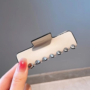 Detail of large cream hair claw clip with black outlines held in hand for scale