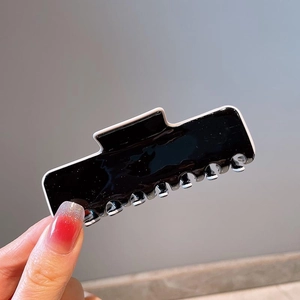Detailed view of large black glossy hair claw clip with white outline being held by hand