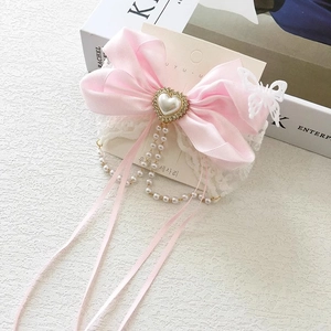 Detail of pink silk bow hairclip with lace trim, pearl heart, and tassel on display card