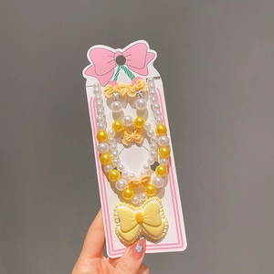 Détail de la parure de bijoux pour enfants avec nœuds jaunes et perles dans l'emballage