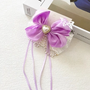 Detailed macro view of purple satin bow hair clip with heart pearl and ribbon tassels