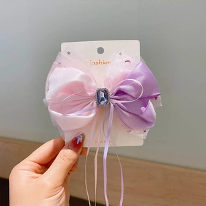Detail of pink and purple mesh bow hair clip with central purple gemstone and long ribbons