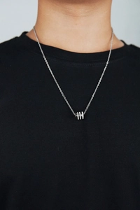 Close-up of a silver cylinder pendant necklace featuring three rows of cubic zirconia stones