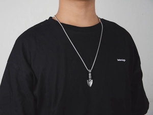 Close-up of hip hop arrow pendant on chain worn by male model over a black t-shirt