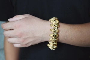 Detailed close-up of a gold-plated hip-hop skull bracelet worn on a model's wrist