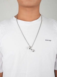 Macro shot of a silver dumbbell pendant necklace worn on a plain white T-shirt