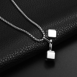 Macro detail of silver dumbbell pendant with stainless steel box chain on leather background