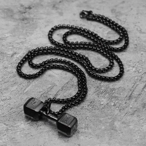 Macro shot of black stainless steel dumbbell pendant showing engraved texture and sturdy chain