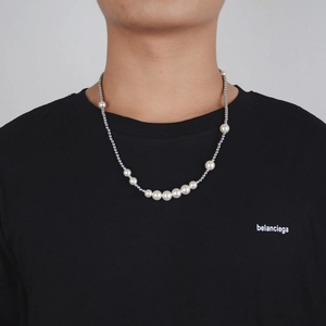 Detail of gradient pearl and silver metal bead necklace worn on a black crew neck