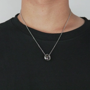 Détail du pendentif à trois anneaux argentés entrelacés porté sur un t-shirt noir