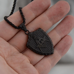Détail macro d'un pendentif bouclier maçonnique noir avec compas et équerre sur fond maillé