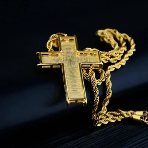Détail d'un grand pendentif croix dorée avec cadre creux et chaîne en corde torsadée