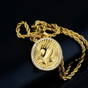 Macro shot of gold hip hop pendant with praying hands and cubic zirconia stone border
