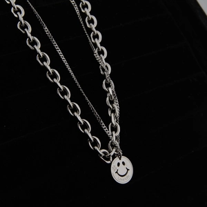 Macro view of layered silver smiley face pendant necklace on black jewelry tray