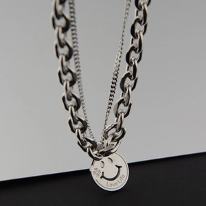 Macro view of silver layered chain necklace with engraved smiling face and clover pendant