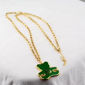 Collier doré avec pendentif ours vert et logo B sur un fond de tissu blanc texturé