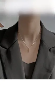 Close-up of minimalist silver cross pendant necklace worn by a model in a dark blazer