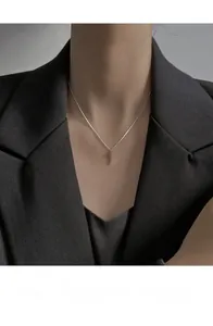 Close-up of minimalist silver cross pendant on a thin chain worn with a black suit