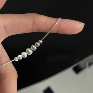Detail of silver snake chain necklace featuring seven graduated brushed metal beads
