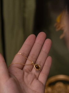 Détail d'un pendentif ovale en ambre argent s925 doré tenu à la main avec sa chaîne