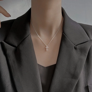 Minimalist silver cross pendant necklace for women in punk style worn on a grey blazer