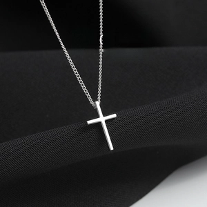 Minimalist silver cross pendant necklace with fine chain on black textured background