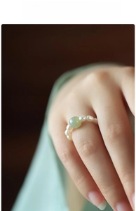Detailed close-up of a vintage Chinese style pearl ring with a green jade bead on a model finger