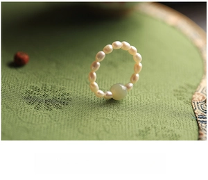 Macro detail of a pearl beaded ring with a central green jade stone on green silk background
