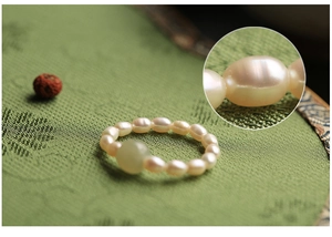 Close-up of Chinese vintage style pearl ring with a green jade bead and silk background