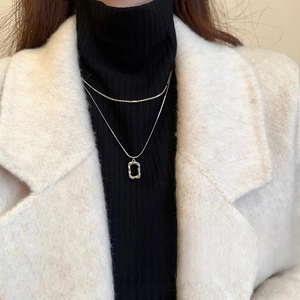 Detail of double-layer gold geometric pendant necklace on a black and white outfit