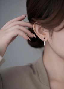 Detailed view of a silver feather earring with a black stone on a female model