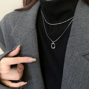 Close-up of double-layer silver geometric pendant necklace on a black turtleneck sweater