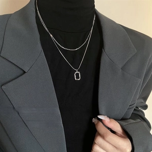 Detail of silver double-layered geometric pendant necklace worn over a black sweater