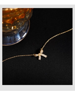 Macro shot of gold bow pendant with white crystals on 925 silver chain over black fabric